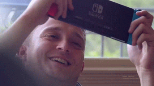 A Man Is Holding A Nintendo Switch In His Hand . GIF