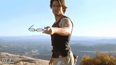 A Man Is Holding A Pair Of Glasses In Front Of A Poster For Mission Impossible 2 GIF