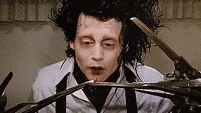 A Man Is Holding A Pair Of Scissors In His Hand . GIF