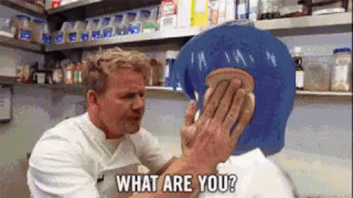 A Man Is Holding A Piece Of Bread Over Another Man 'S Face And Asking What Are You ? GIF