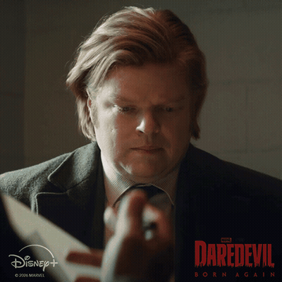 A Man Is Holding A Piece Of Paper In Front Of A Daredevil Born Again Poster GIF
