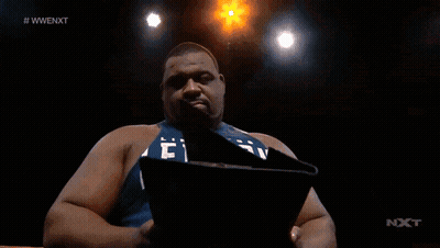 A Man Is Holding A Piece Of Paper In Front Of A Screen That Says #Wwenext GIF