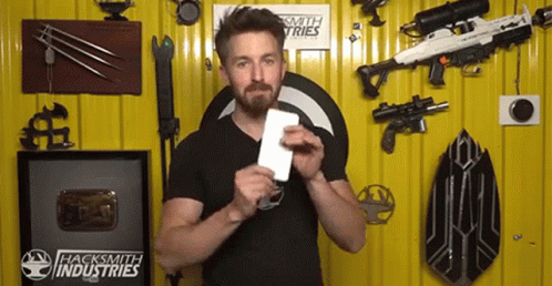 A Man Is Holding A Piece Of Paper In Front Of A Wall That Has Hacksmith Industries Written On It GIF