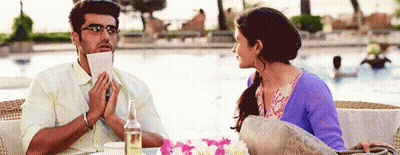 A Man Is Holding A Piece Of Paper In His Mouth And A Woman Is Looking At Him GIF