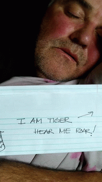 A Man Is Holding A Piece Of Paper That Says I Am Tiger Roar Hear Me GIF
