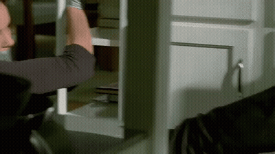 A Man Is Holding A Piece Of Wood In His Hand While Standing In Front Of A Cabinet . GIF
