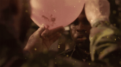 A Man Is Holding A Pink Balloon Over His Head With Flowers On It GIF