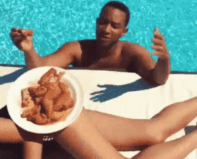 A Man Is Holding A Plate Of Chicken Wings Over A Woman 'S Legs GIF