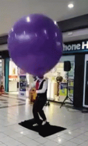 A Man Is Holding A Purple Balloon In Front Of A Store Called Home GIF