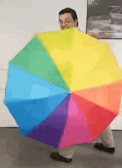 A Man Is Holding A Rainbow Colored Umbrella In Front Of Him GIF