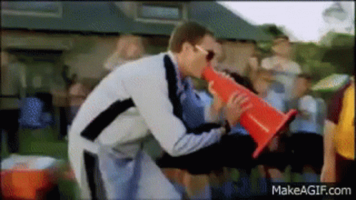 A Man Is Holding A Red Cone In His Hand And Blowing Into It GIF