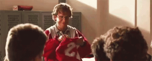 A Man Is Holding A Red Jersey With The Number 2 On It In Front Of A Group Of People . GIF