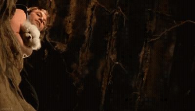 A Man Is Holding A Small White Dog In His Arms While Climbing Up A Tree . GIF