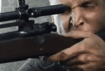 A Man Is Holding A Sniper Rifle In His Hand And Looking Through The Scope . GIF