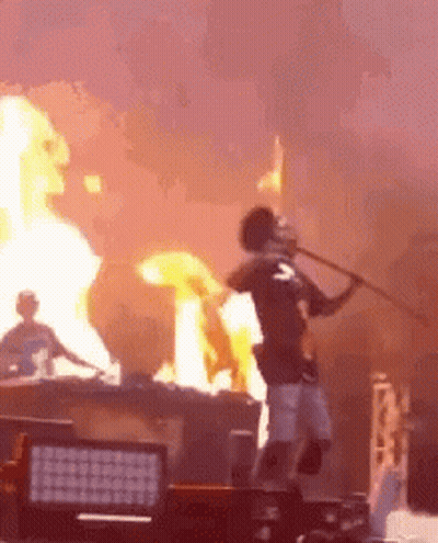 A Man Is Holding A Stick In Front Of A Fire While Standing On A Stage . GIF