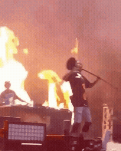 A Man Is Holding A Stick In Front Of A Fire While Standing On A Stage . GIF