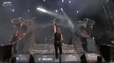 A Man Is Holding A Sword In Front Of A Monster Logo On A Stage GIF