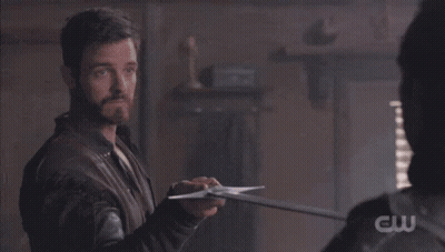 A Man Is Holding A Sword In Front Of Another Man With A Cw Logo Visible GIF