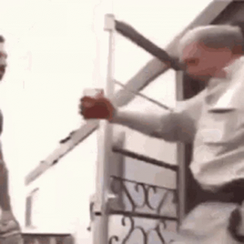 A Man Is Holding A Sword In His Hand While Standing Next To A Building . GIF