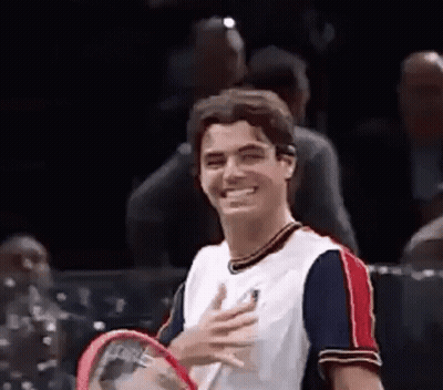 A Man Is Holding A Tennis Racquet And Smiling While Standing On A Tennis Court . GIF