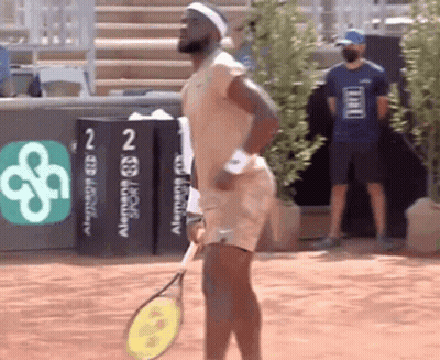 A Man Is Holding A Tennis Racquet In Front Of A Sign That Says ' Alemania Sport ' On It GIF