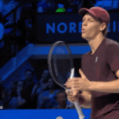 A Man Is Holding A Tennis Racquet In Front Of A Sign That Says Nor GIF