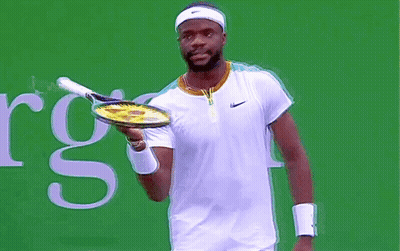 A Man Is Holding A Tennis Racquet In Front Of A Sign That Says Rgs GIF