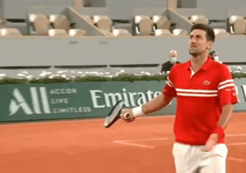 A Man Is Holding A Tennis Racquet In Front Of An Emirates Sign GIF