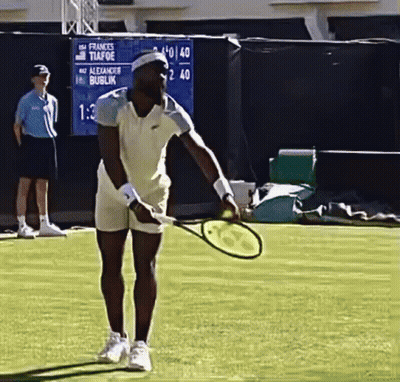 A Man Is Holding A Tennis Racquet On A Court With A Scoreboard Behind Him That Says Frances Tiafoe GIF