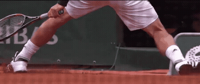 A Man Is Holding A Tennis Racquet On A Red Court GIF