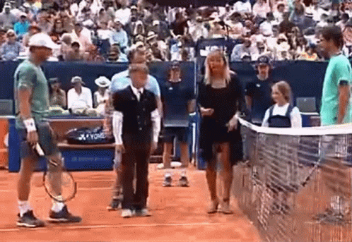 A Man Is Holding A Tennis Racquet While Standing On A Tennis Court Next To A Woman . GIF