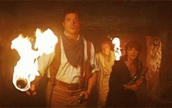 A Man Is Holding A Torch In A Dark Room While A Group Of People Are Standing Behind Him . GIF