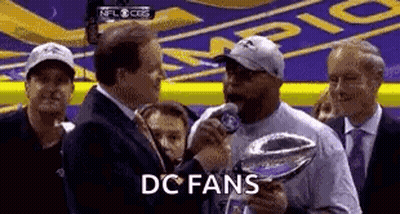 A Man Is Holding A Trophy And Talking Into A Microphone In Front Of A Crowd . GIF