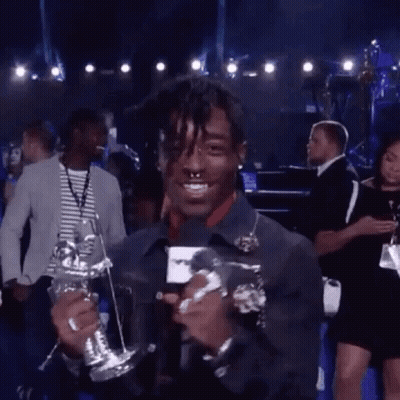 A Man Is Holding A Trophy And Talking Into A Microphone While Standing On A Stage . GIF