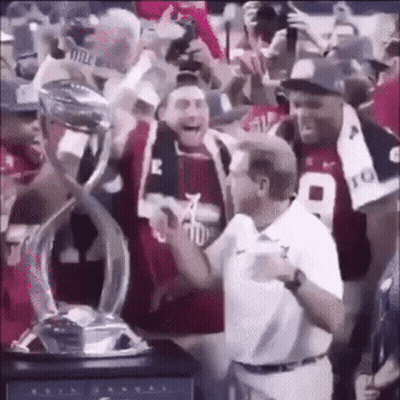 A Man Is Holding A Trophy In A Crowd Of People . GIF