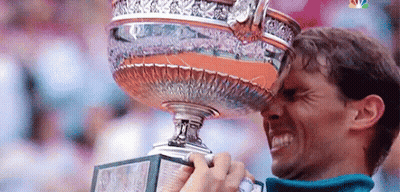A Man Is Holding A Trophy In His Hand And Kissing It On His Forehead . GIF