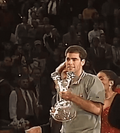 A Man Is Holding A Trophy In His Hands In Front Of A Crowd Of People . GIF
