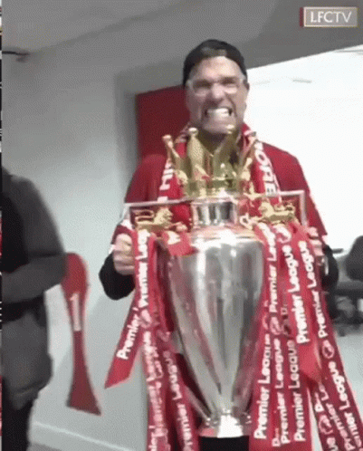A Man Is Holding A Trophy With Red Ribbons Around It And Making A Funny Face . GIF