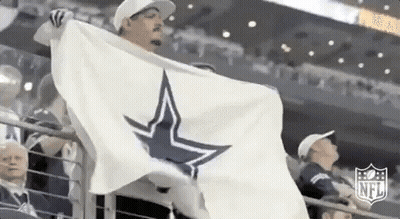 A Man Is Holding A White Flag With A Cowboys Star On It In A Stadium . GIF
