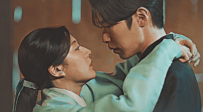 A Man Is Holding A Woman In His Arms And Kissing Her . GIF
