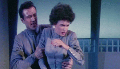 A Man Is Holding A Woman In His Arms And She Is Looking At Him GIF