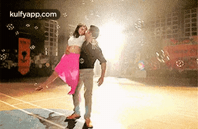 A Man Is Holding A Woman In His Arms On A Basketball Court Surrounded By Bubbles . GIF