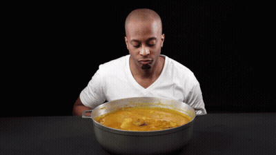 A Man Is Holding A Wooden Spoon In Front Of A Pot Of Soup GIF