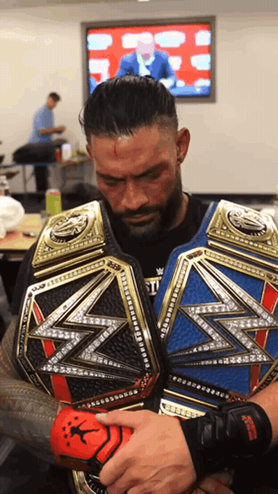 A Man Is Holding A Wrestling Belt In Front Of A Television Screen GIF