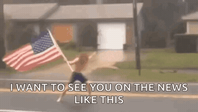 A Man Is Holding An American Flag On The Side Of The Road . GIF