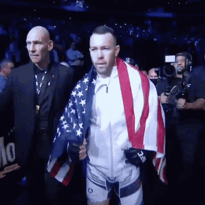 A Man Is Holding An American Flag While Walking Through A Stadium . GIF