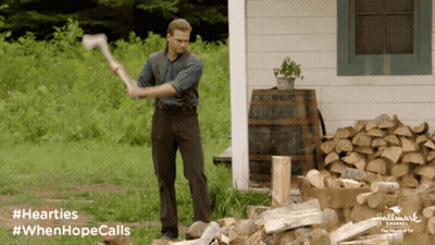 A Man Is Holding An Axe In Front Of A Pile Of Logs And A Sign That Says Hallmark Channel GIF