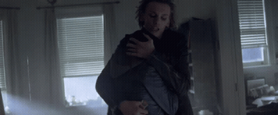 A Man Is Holding Another Man In His Arms In A Room With Blinds GIF
