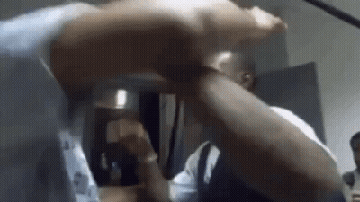 A Man Is Holding Another Man 'S Arm In A Room While They Are Fighting . GIF