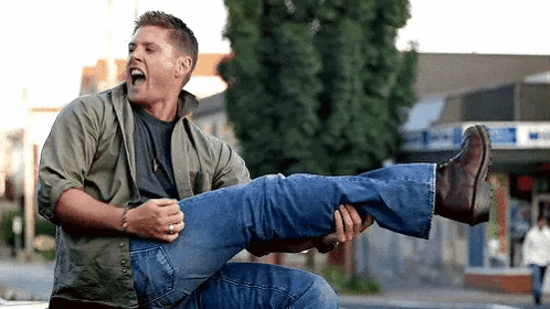 A Man Is Holding Another Man 'S Leg In His Arms While Sitting On The Back Of A Car . GIF